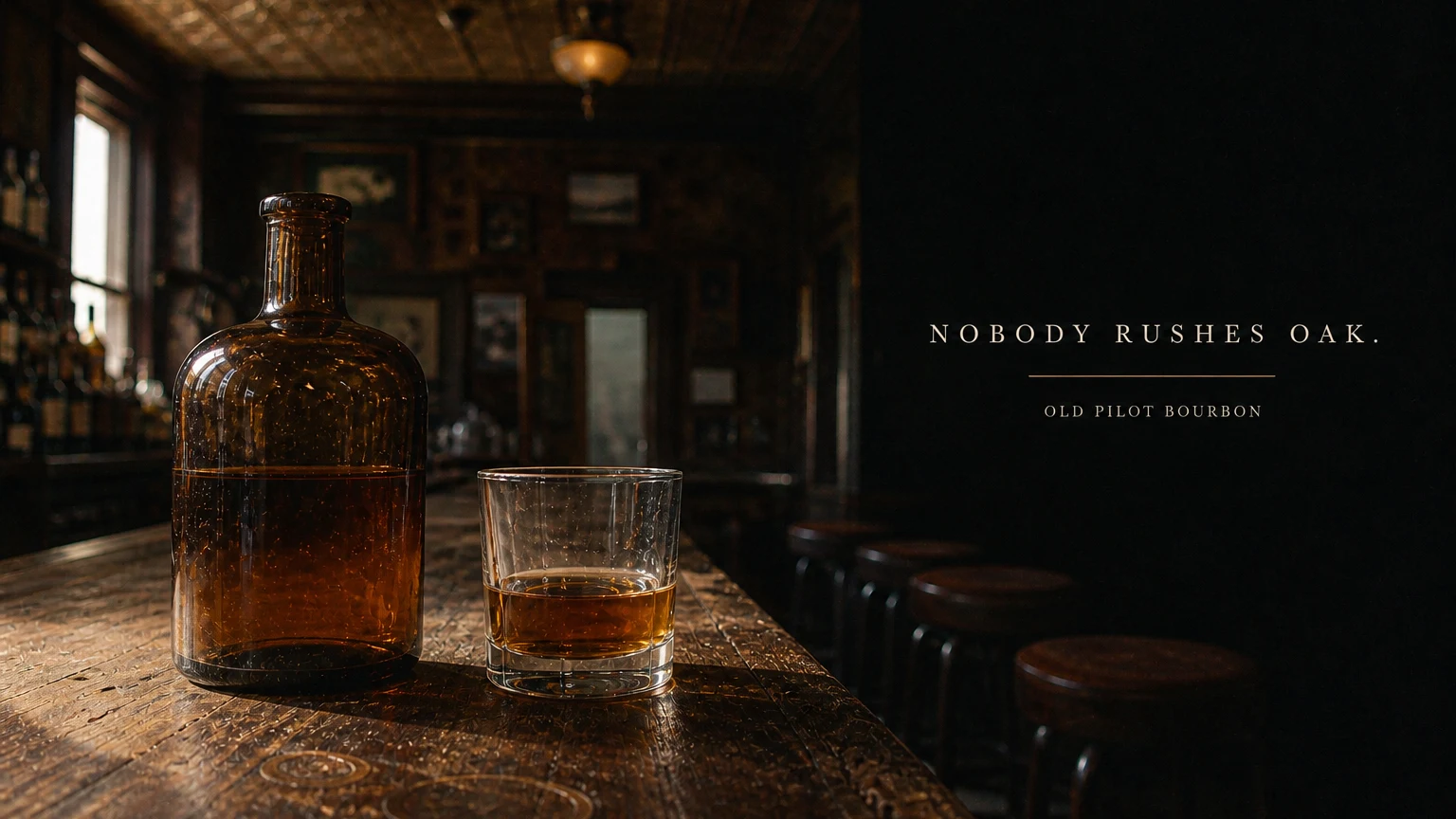 An unlabeled amber bottle and a poured rocks glass on a scarred bar top in late light, a wide serif line set in the dark right third.