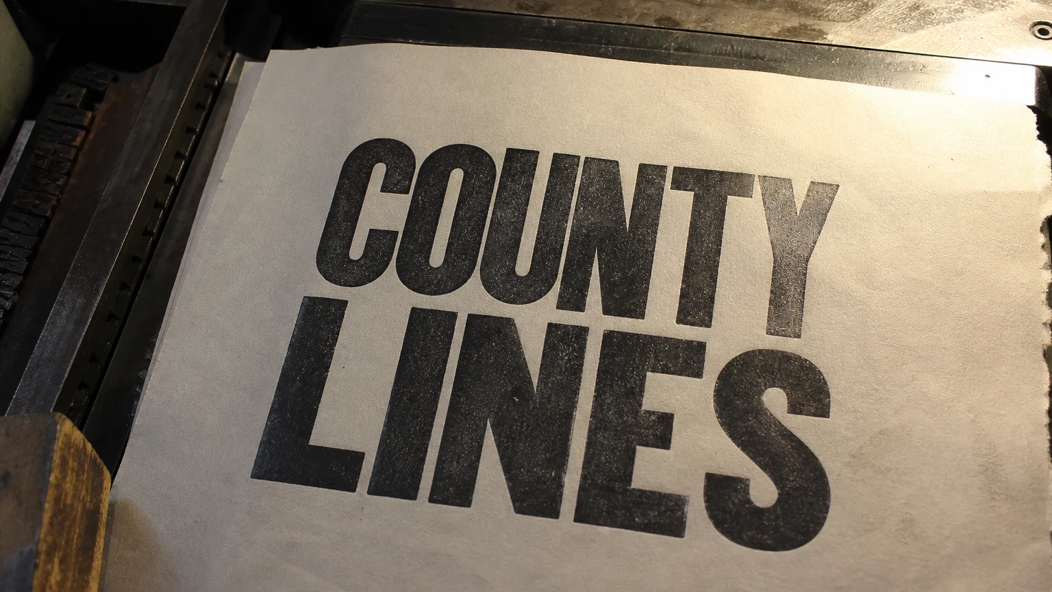 A letterpress proof on the press bed, heavy wood-type capitals pressed deep into newsprint.